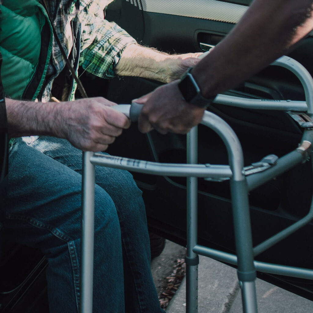 Un homme aide une personne âgée à sortir d'une voiture durant l'accompagnement véhiculé