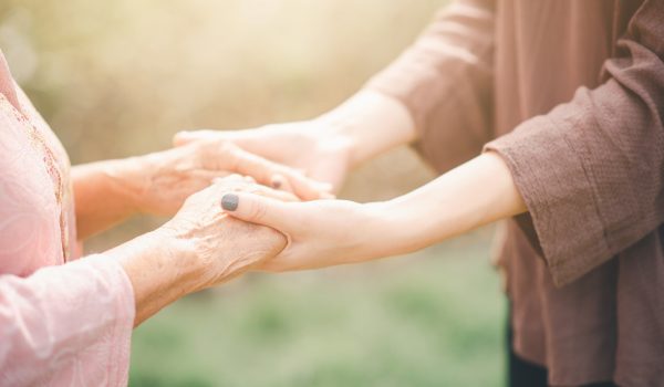 Vieille et jeune femme se tenant la main avec soin sous la lumière du soleil