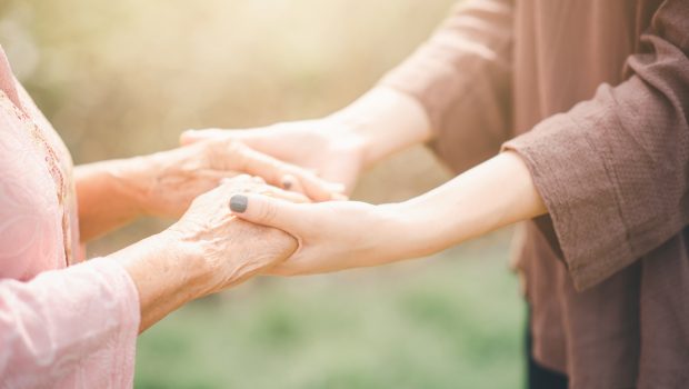 Vieille et jeune femme se tenant la main avec soin sous la lumière du soleil