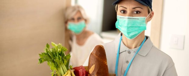 Femme avec un masque livrant un sac d'aliments à une personne âgée